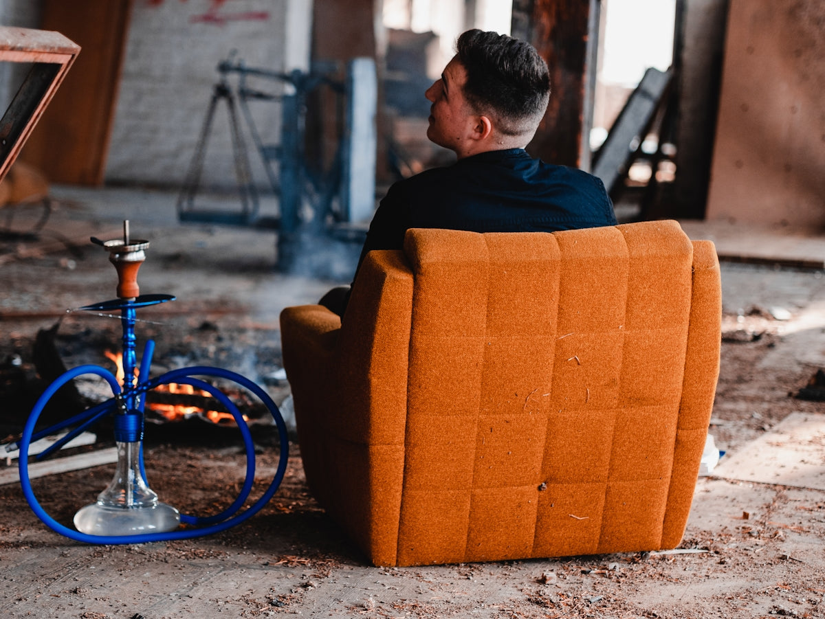 man sitting on brown suede padded sofa beside gray and blue hookah