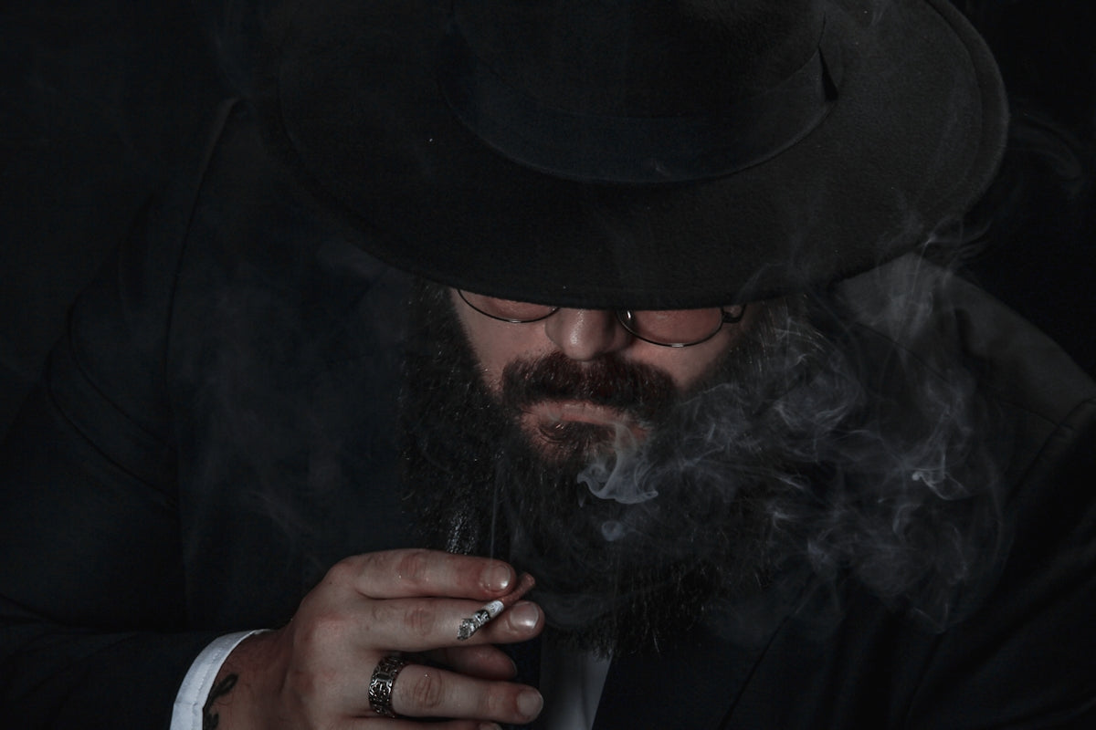 a man in a suit and hat smoking a cigarette