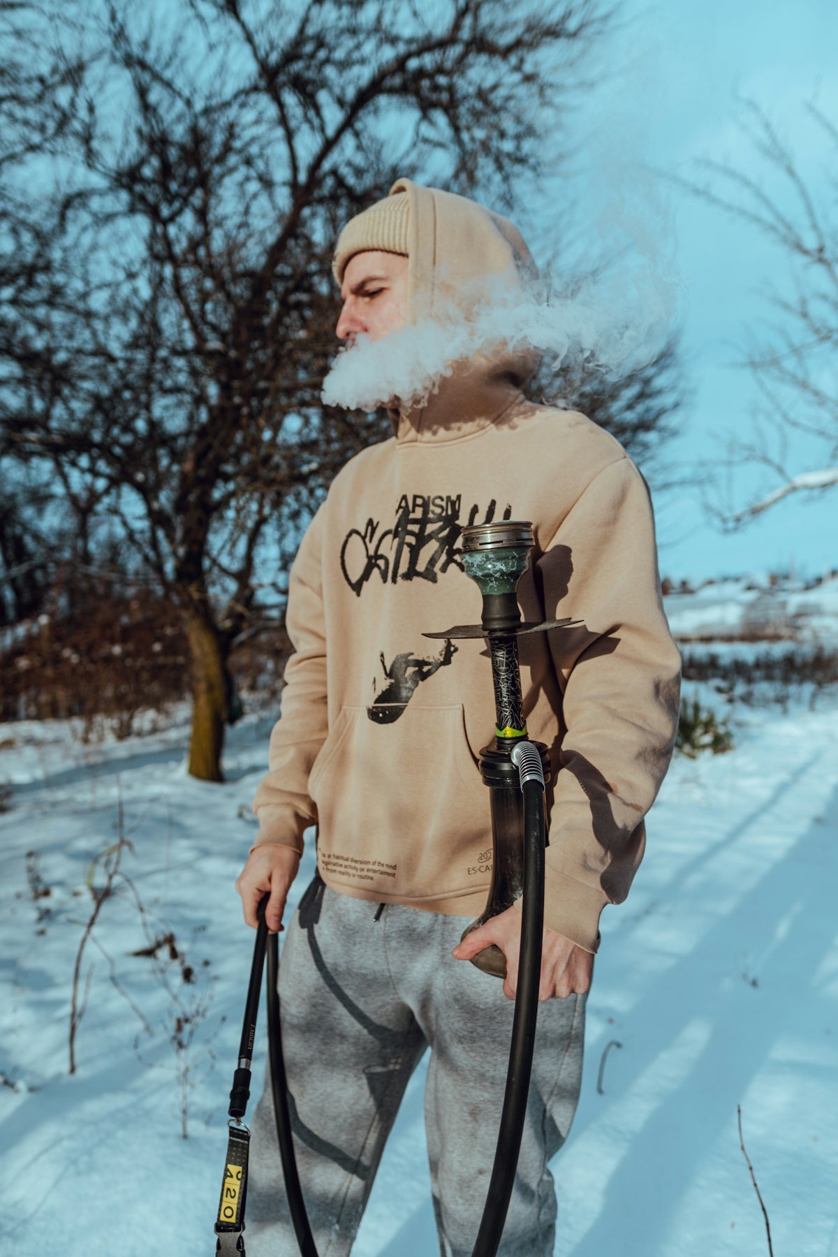 Man exhales smoke while holding a hookah in snow.